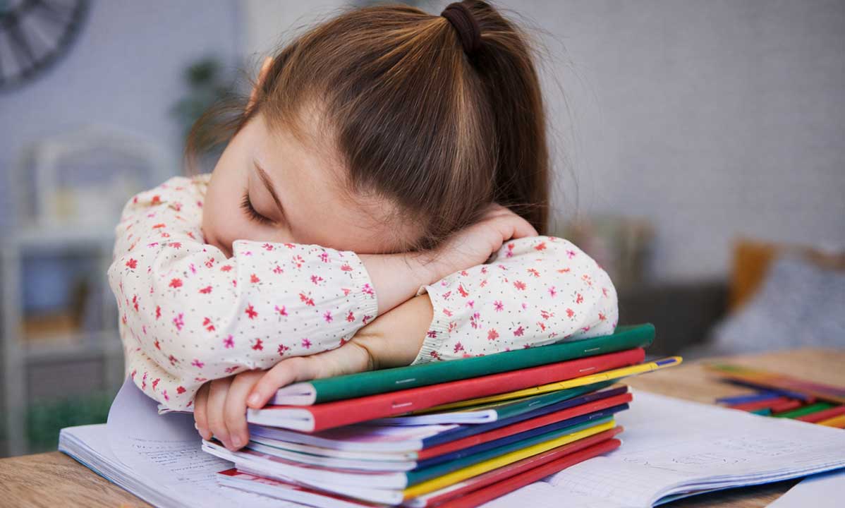 Müdes Kind mit ADHS sitzt über Hausaufgaben und hat Schwierigkeiten sich zu konzentrieren