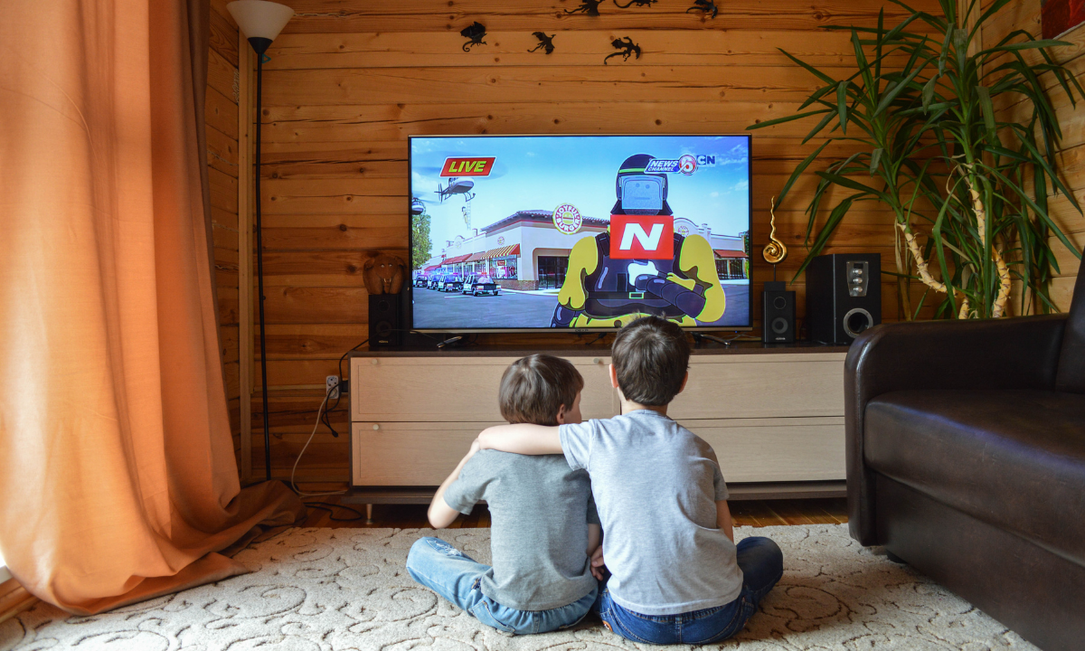 Zwei Kinder sitzen auf dem Wohnzimmerboden und schauen gemeinsam fern.